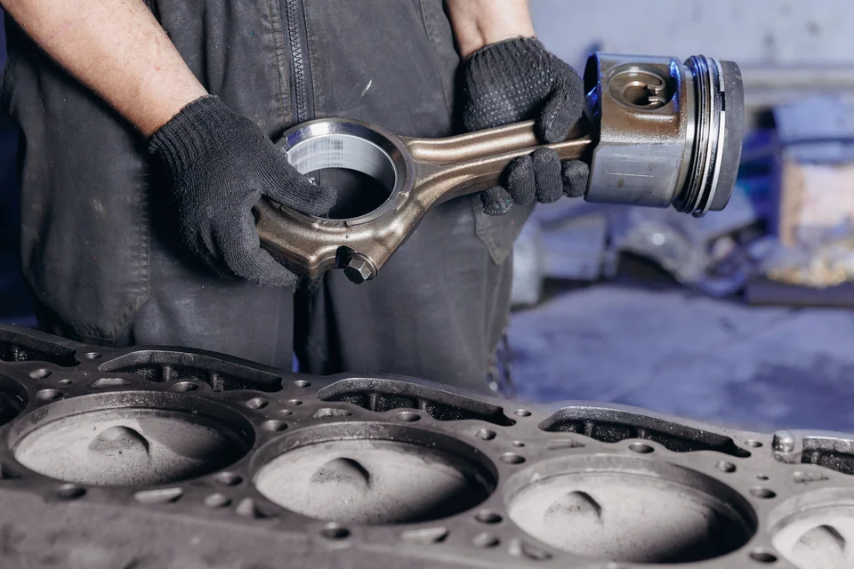 Illustrative Aufnahme: Mechaniker hält einen Kolben über einem Motorblock